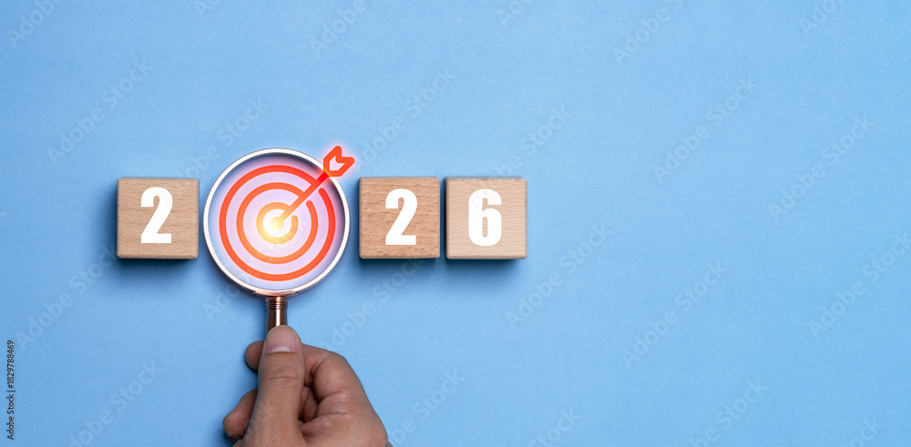 Naklejka premium Hand holding magnifying glass highlighting a target icon between the numbers 2026 represents a happy new year with focus goal setting motivation precision planning and direction for future success.