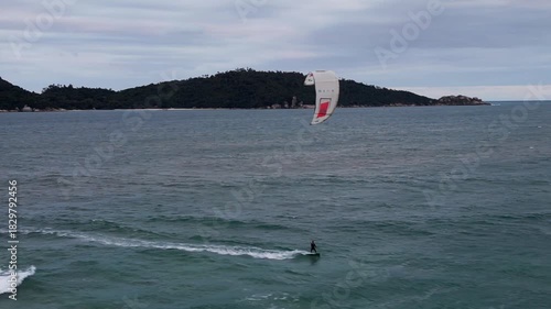 Energetic aerial view of a kitesurfer gliding smoothly over waves, blending motion and coastal atmosphere.