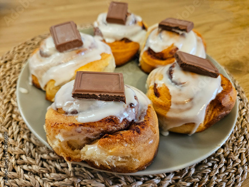 Closeup of freshly baked sweet and delicious cinnamon buns topped with white icing and a square of milk chocolate.