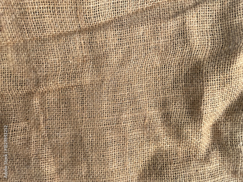 Natural burlap fabric close-up texture. Beige woven jute material with visible fibers and folds. Rustic background perfect for packaging design, crafts, textiles, eco style, and mockups.
