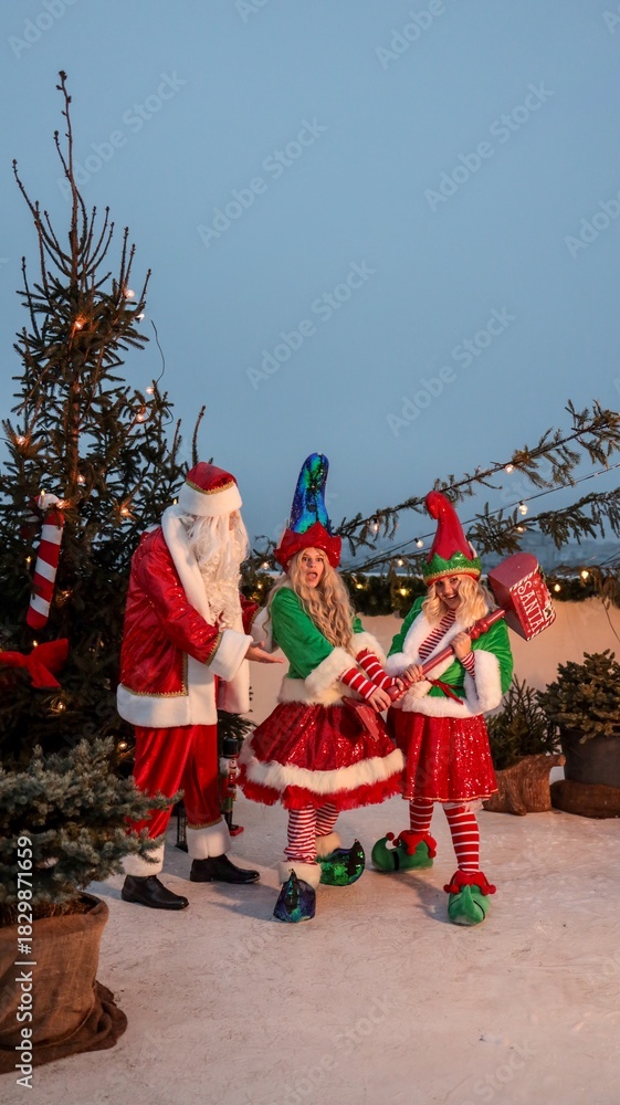 Naklejka premium Santa Claus with elves in a festive Christmas scene with a hammer