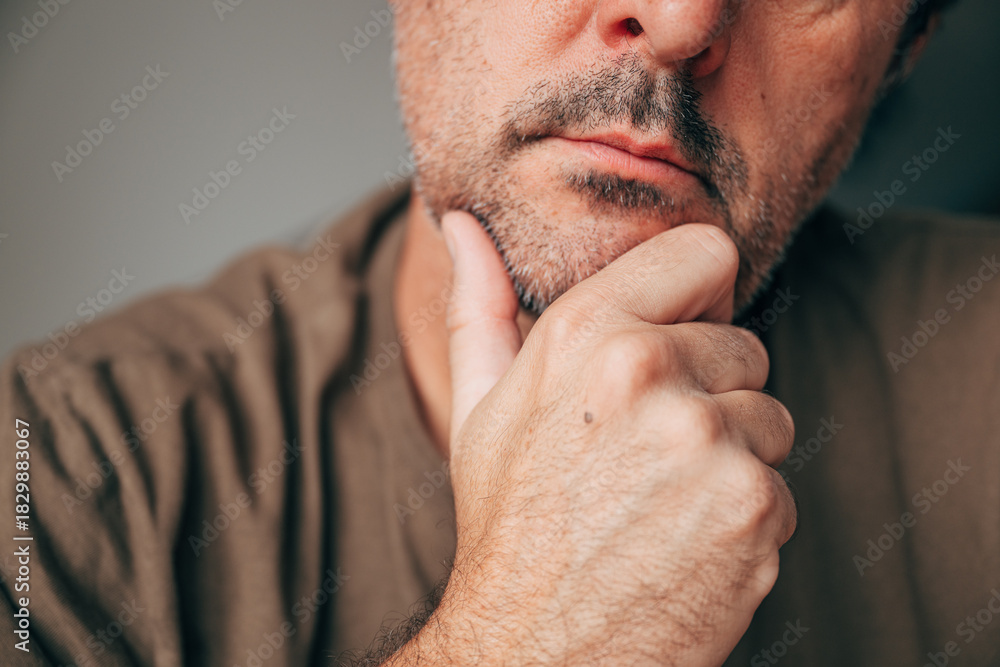 Fototapeta premium Closeup of thoughtful mature man touching chin, concept of contemplation and decision making. Pensive adult male in casual clothing with hand on chin, symbolic of reflection and problem solving.