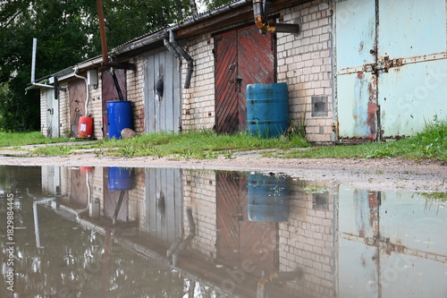Lettland: Eine Reihe rustikaler Hinterhofgaragen spiegelt sich in einer Wasserpfütze