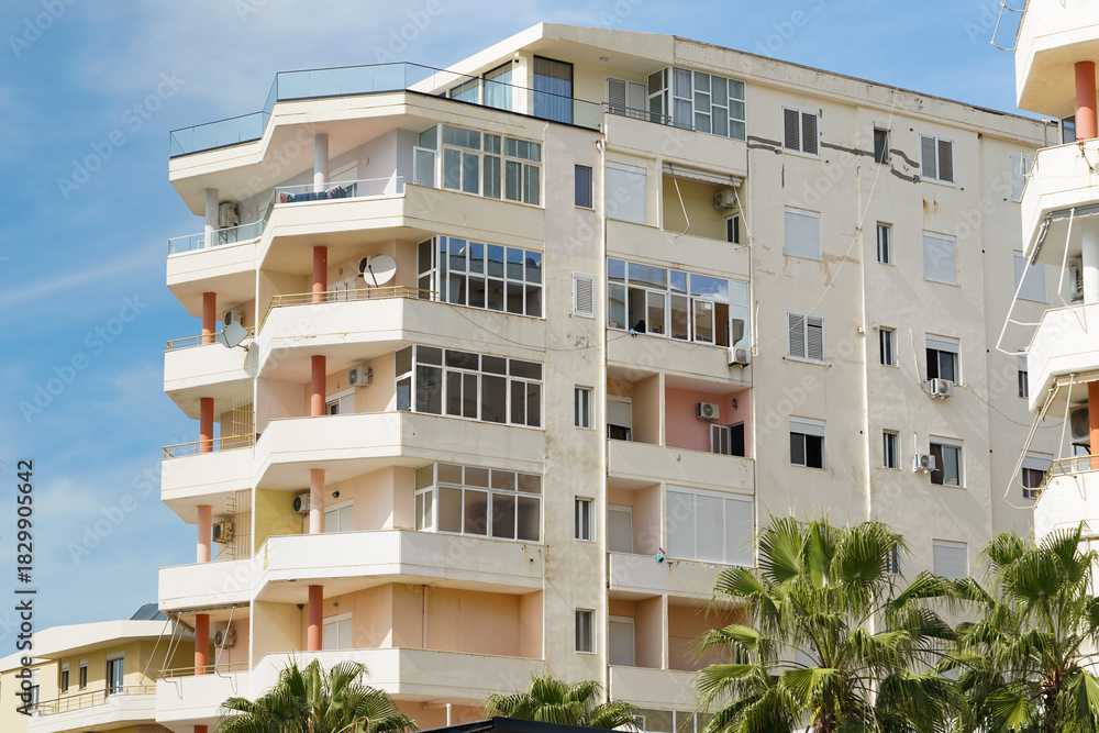 Fototapeta premium Bright Mediterranean house with pastel walls and stone balconies stands on quiet Albanian street. Concept of coastal real estate, long-term rentals, and relaxed seaside living.