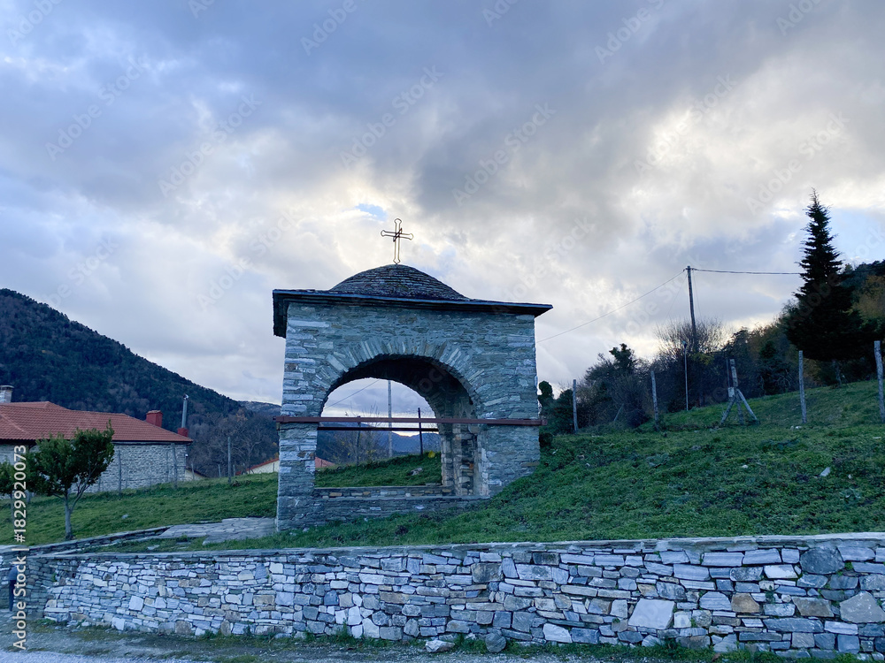 Obraz premium Rustic stone archway with cross set against serene mountain landscape at dusk