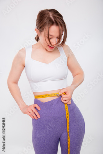 Beautiful sports girl measuring her waist with a measure tape isolated on a white background. Attractive young woman in sportswear posing in the studio.