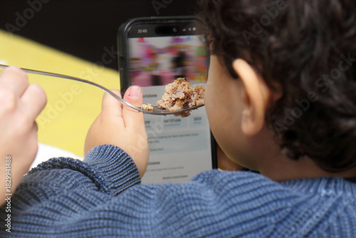 Child watching smartphone cartoon while being fed food with a fork