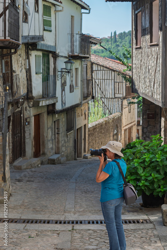Female tourist seen from behind photographing the streets of the villages of the Sierra de Francia (Salamanca, Spain) in summer