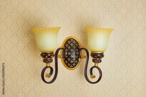 Close-up of double brown lamp on wall with yellow wallpaper.