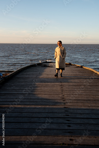 Woman contemplating sunset over sea from pier. Whitstable Kent United Kingdom