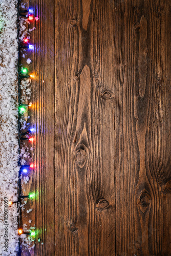 Christmas background featuring a rustic wooden surface decorated with snow and colorful glowing string lights