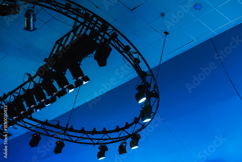 A circular truss lighting rig suspended from the ceiling casts blue tones