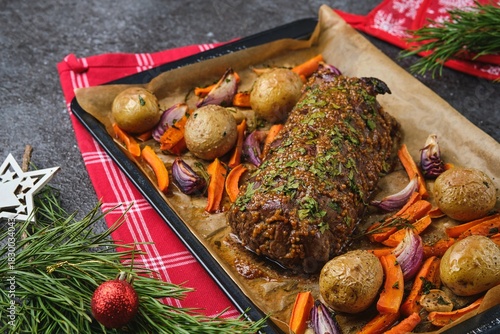 A roast beef loin on a baking sheet with carrots, onions, and potatoes. Cooking beef in the oven as a whole piece. Merry Christmas.
