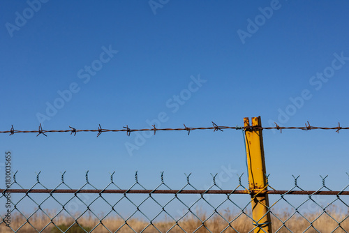 Barbed wire fence against blue sky. Symbol of prison, border protection, safety, defense, and immigration control