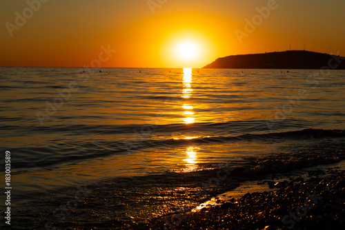 Mediterranean harbor at sunset in Albania. Orange sky over blue sea, waves and mountain. Concept of travel, tourism and vacation