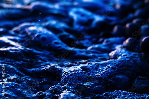 Closeup sea foam and bubbles on blue water surface. Abstract cool ocean background, natural macro texture for summer, travel, refreshment and nature concepts