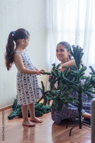 Madre e hija sonriendo y armando un árbol de Navidad