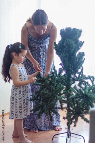 Madre guiando a su hija en la decoración del árbol de navidad