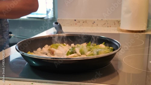 Vegetables are cooking in the pan, turned with a wooden spatula to prevent burning.