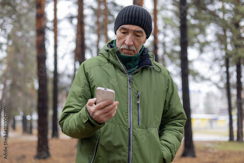 An elderly man in the forest with a phone. Concept of cellular communication and navigation in the forest.