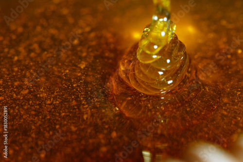 Golden honey dripping slowly into a pool of amber liquid, showcasing the smooth texture and rich color, highlighting the natural sweetness and culinary versatility of honey
