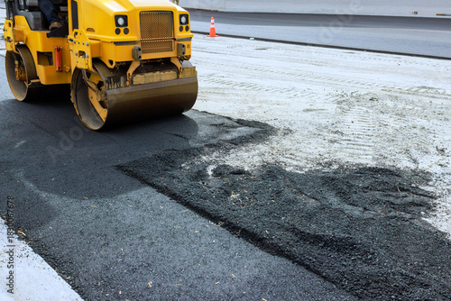 Heavy machinery is actively smoothing asphalt on city road preparing for new surface work.