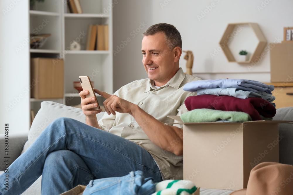 © Pixel-Shot - Mature man using mobile phone while unpacking box with clothes at home © Pixel-Shot - Mature man using mobile phone while unpacking box with clothes at home