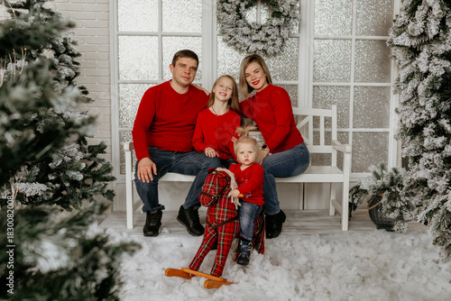 Family of four sitting on a white bench, with the youngest child riding a rocking horse, surrounded by snow and Christmas decorations