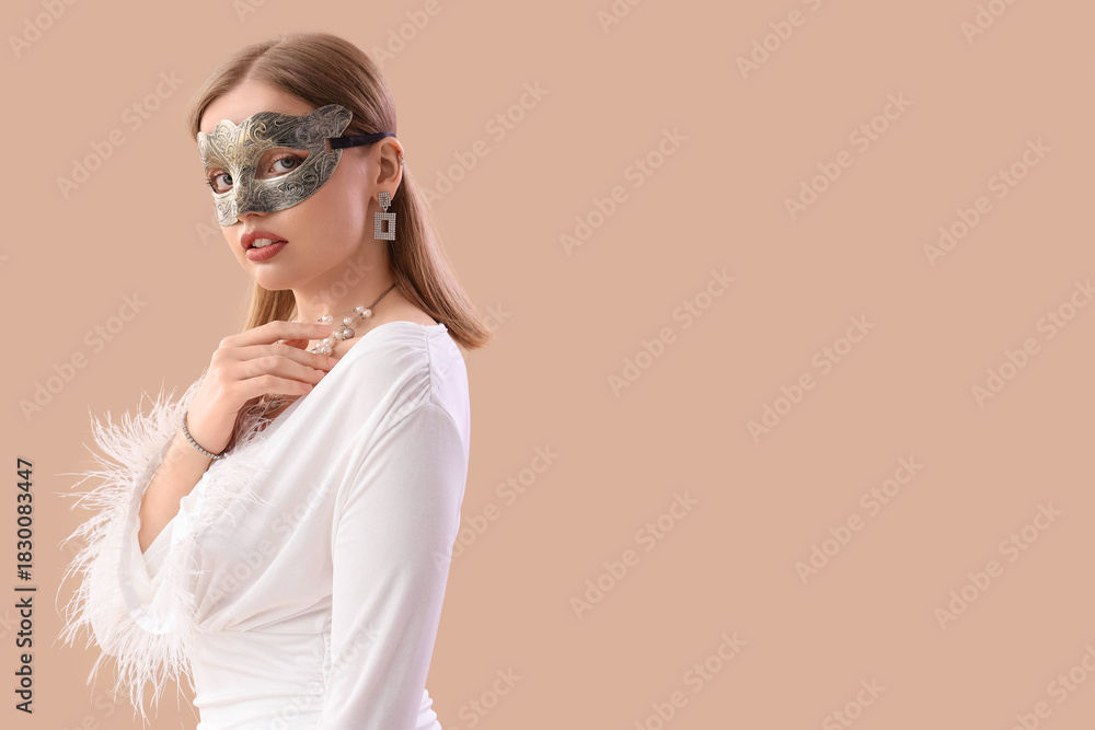 Fototapeta premium Beautiful young woman wearing carnival mask on beige background