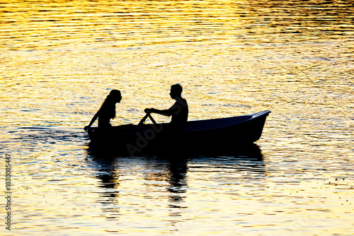silhouette of people in boats with oars on the evening river