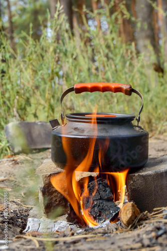 black camping kettle heating on fire in nature, vertical frame