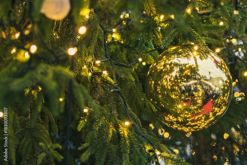 Close-up detail of a Christmas tree with a shiny golden bauble, surrounded by twinkling lights and green pine needles