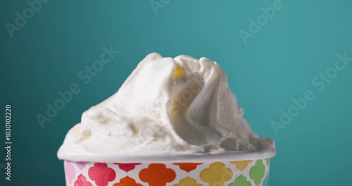 white soft vanilla ice cream in paper cup rotating, food closeup on blue background