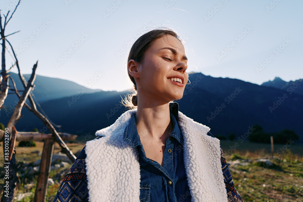 Fototapeta premium Woman portrait in mountains nature at golden sunlight, smiling and happy outdoors with casual jacket and wool vest, scenic landscape background and peaceful rural vibe during sunset.
