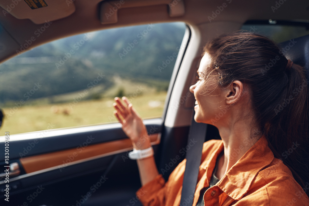 Naklejka premium Woman seated in a car, gazing out the window at a scenic landscape, enjoying a peaceful travel moment under bright daytime light in a moving road setting.