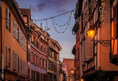 Fototapeta Naklejka Na Ścianę i Meble -  Christmas decorations on half timbered houses in Colmar, France glow at sunset