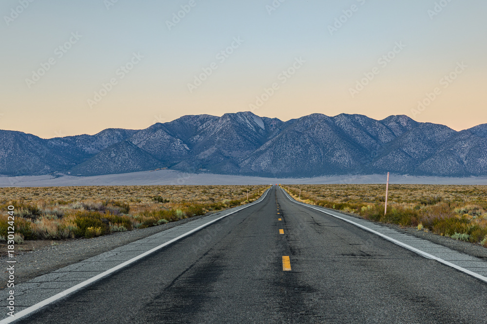 Naklejka premium Iconic straight stretch of Freeway at sunset, leading directly toward dramatic eastern escarpment of the Sierra Nevada across the vast high-desert plain near Hot Creek, California.