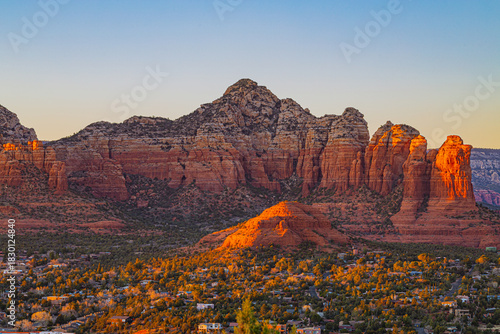 Majestic red sandstone formations tower above the town of Sedona at dusk. The soft evening light highlights the rugged cliffs and desert terrain of northern Arizona.