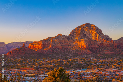 A warm golden-hour view of Sedona, Arizona, with dramatic red rock formations glowing under sunset light and the town below.
