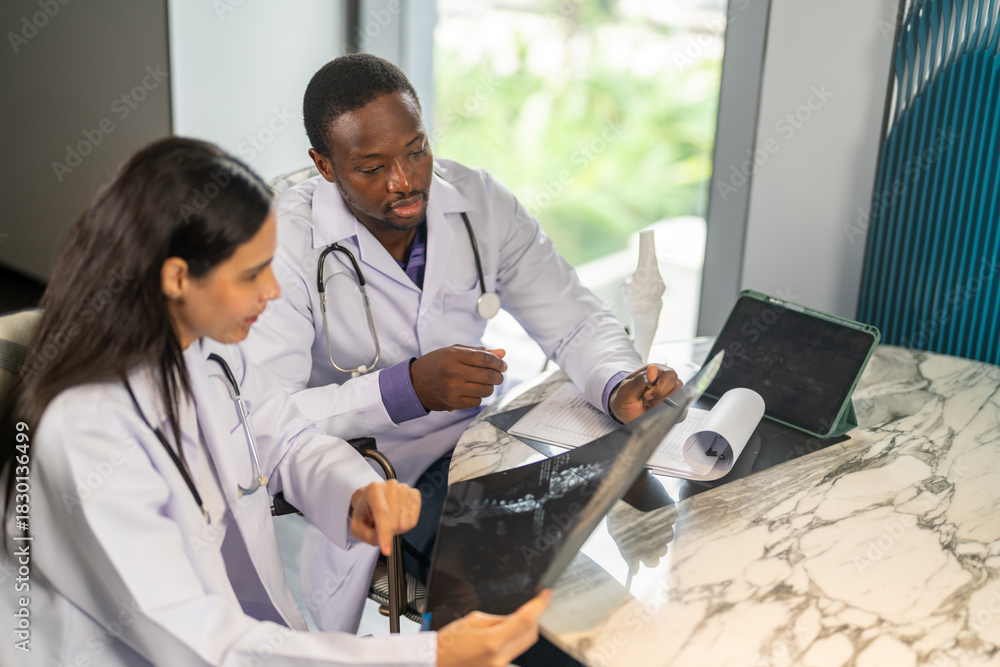Obraz premium Diverse medical team african male doctor and female doctor collaborating and reviewing medical documents writing and discussing patient data in hospital office, teamwork in healthcare, patient care
