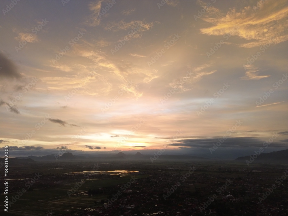 Fototapeta premium Epic sunset with orange and pink clouds above a vast landscape, blending warm tones with dramatic shadows for a striking atmospheric scene.