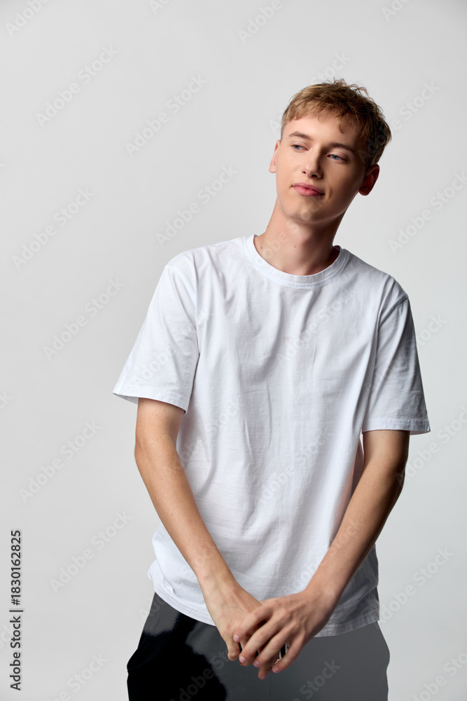 Obraz premium Young man wearing a white t shirt in a simple studio setting, casual and relaxed pose, clean style, emphasis on everyday fashion and comfortable attire
