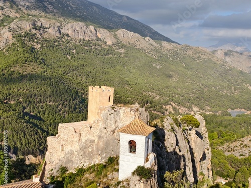 crumbling cliffside chapel adjacent to ancient fortress overlooking ravine with panoramic mountain