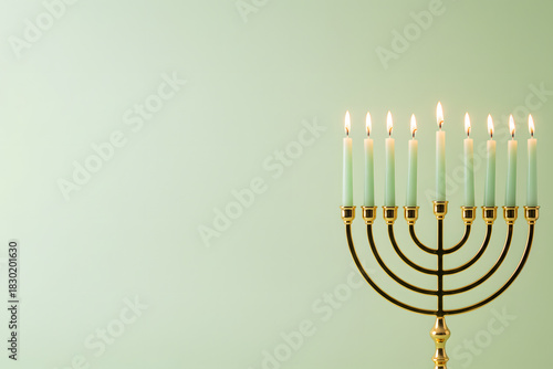 A golden menorah with lit candles stands on a light green background. The image captures Hanukkah celebration, warmth and greeting moments. Tradition, faith, and festive light.