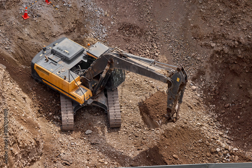  Excavator digging on a construction site, moving soil and rocks during groundwork and foundation preparation.