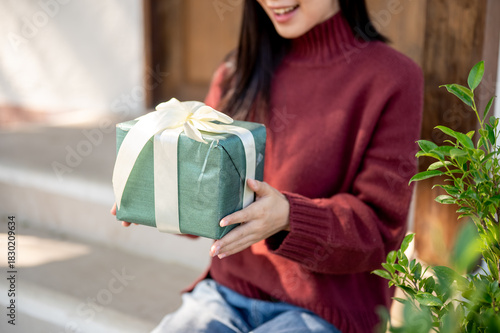Close up woman in red sweater holding at present gift box while sitting in front of home cafe's door