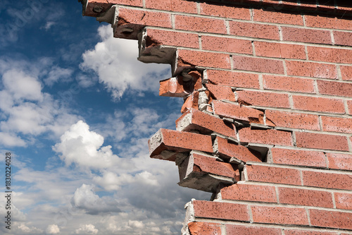 Brocken brick wall and blue sky with white clouds on background