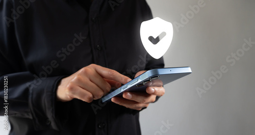 A hand holds a cell phone icon of a shield with a check mark