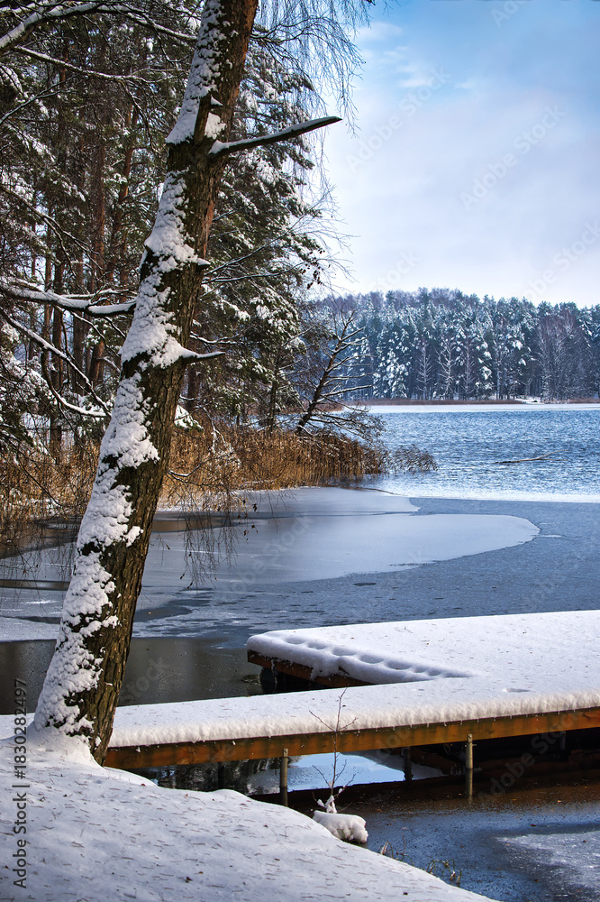 Fototapeta premium Snowy Lakeside Dock Scene With Snow-Covered Trees And Calm Frozen Water