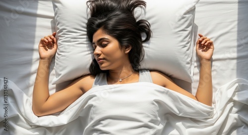 Overhead shot of young Indian female sleeping calmly in bright white sheets